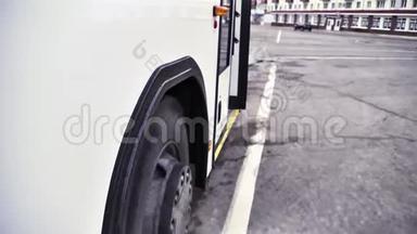 在灰色沥青背景下开始移动的带有巴士轮的白色巴士的侧面视图。 场景。 靠近白色